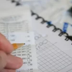 Una mano que sostiene un lápiz repasa un recibo encima de un papel cuadriculado; una calculadora se sitúa cerca, sugiriendo cálculos o presupuestos bajo la guía de la ley de la segunda oportunidad.
